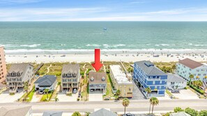 A beachfront hotel with a road in front, a beach with umbrellas, and the ocean in the background.