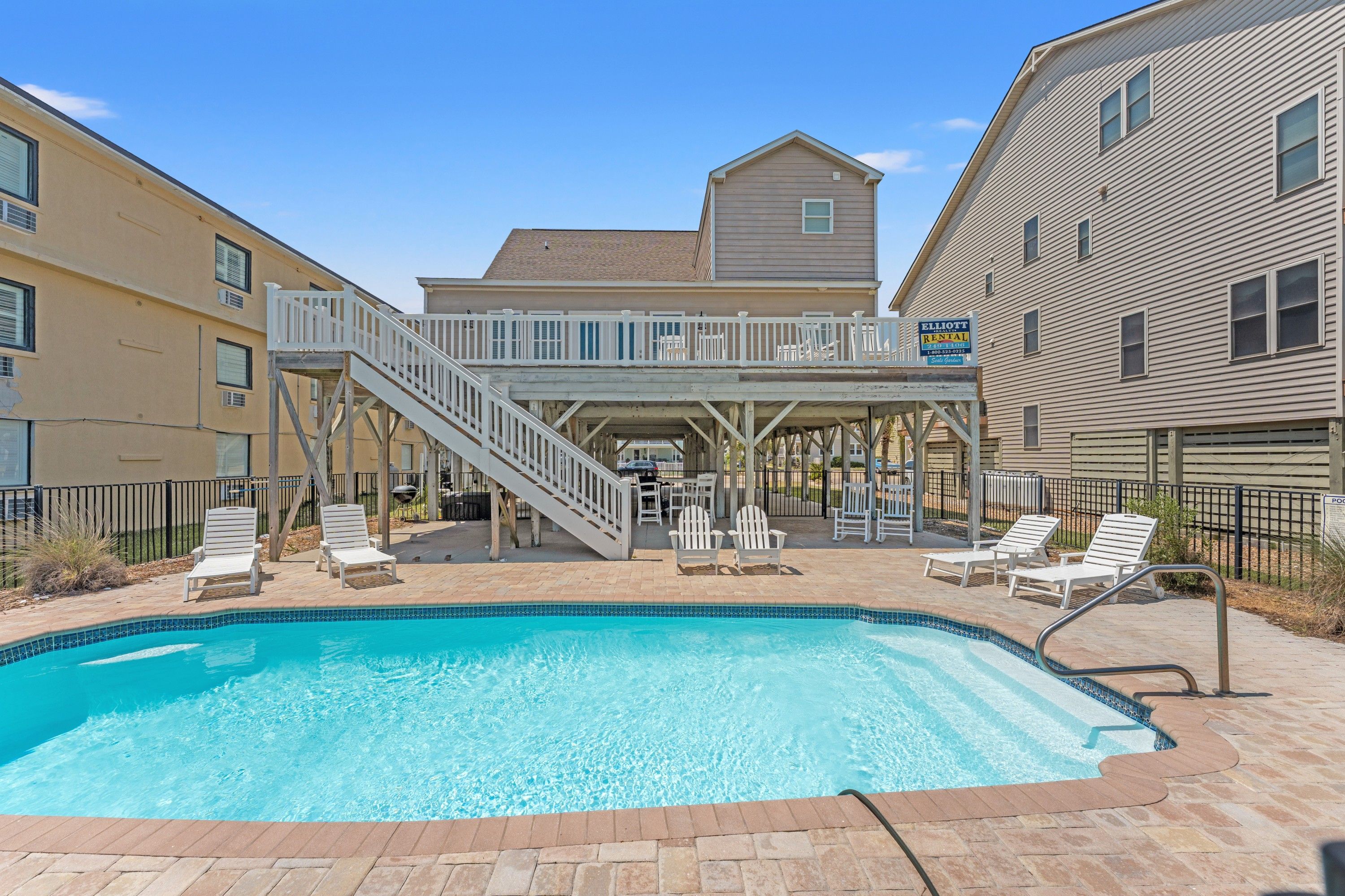 A swimming pool with lounge chairs, a covered deck with stairs, and a rental sign.