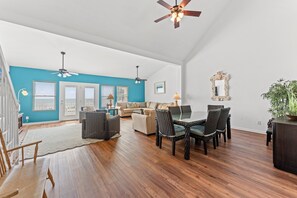 A spacious living room with a blue accent wall, a dining area with wicker chairs, and a ceiling fan.
