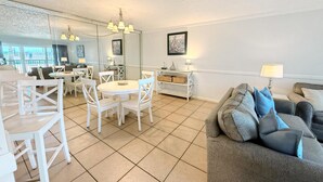 A spacious living area with a dining table and chairs, a gray sofa with blue cushions, and a large mirror reflecting the room. - Moondrifter 105 (Panama City Beach)