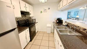 A compact kitchen with white cabinets, a stainless steel sink, a microwave, and a trash bin. - Moondrifter 105 (Panama City Beach)