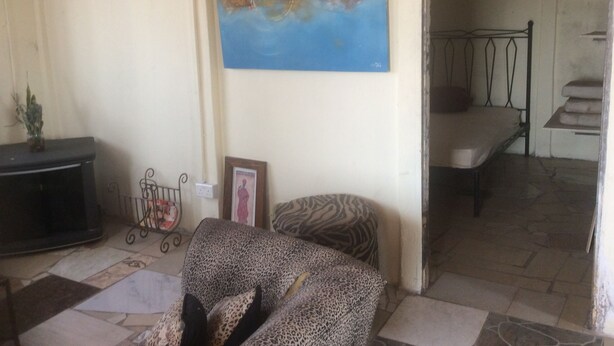 A living room with a sofa, a painting, a small table with a plant, and a staircase leading to an upper floor. - NHAKA Savaal - cottage DETROIT (Harare)