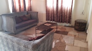A living room with a sofa, a patterned armchair, a coffee table, and a zebra-patterned ottoman. - NHAKA Savaal - cottage DETROIT (Harare)