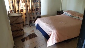 A bedroom with a bed, a small table, a chair, and a patterned curtain. - NHAKA Savaal - cottage DETROIT (Harare)