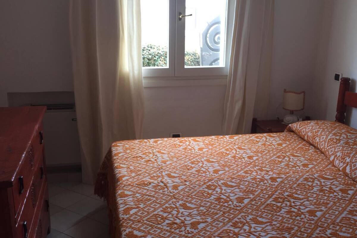 Une chambre à coucher avec un lit, une commode, une fenêtre avec des rideaux et une table de chevet avec une lampe.