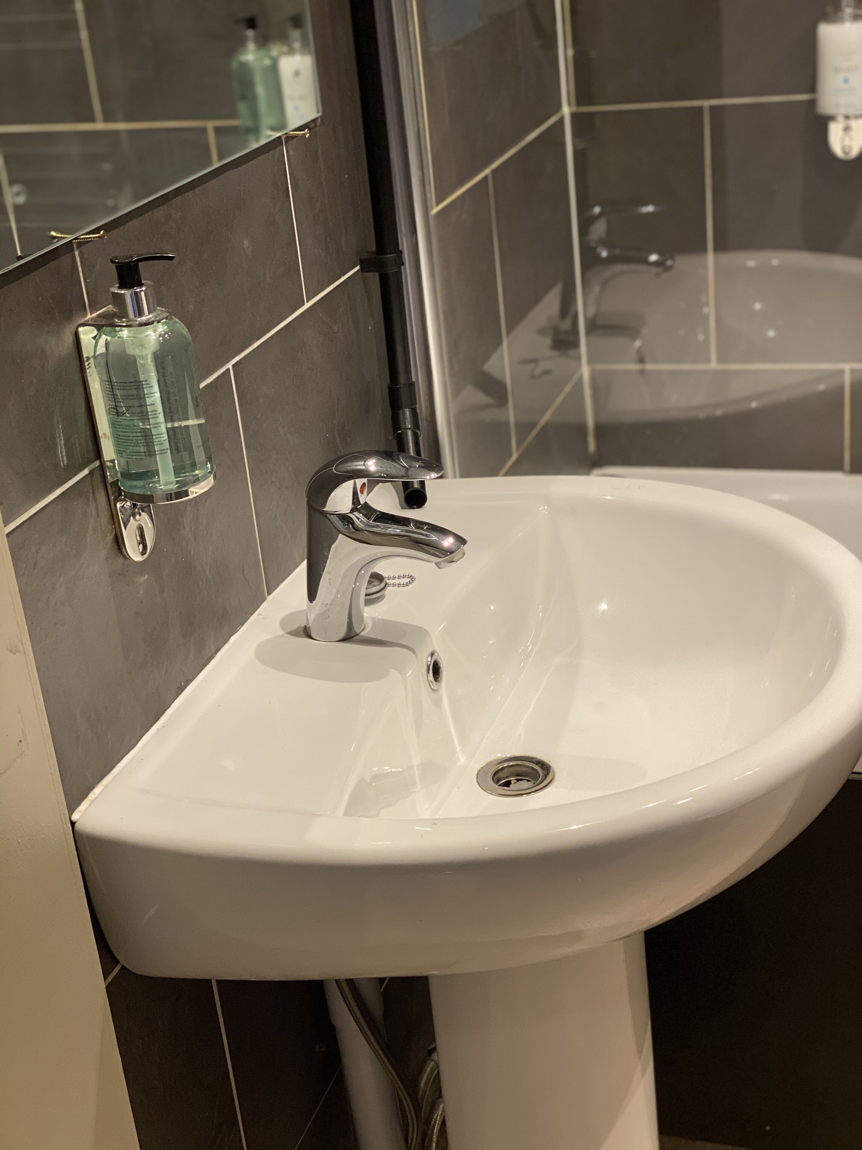 Un lavabo blanc dans une salle de bain, avec un robinet chromé, un distributeur de savon et un miroir au-dessus.
