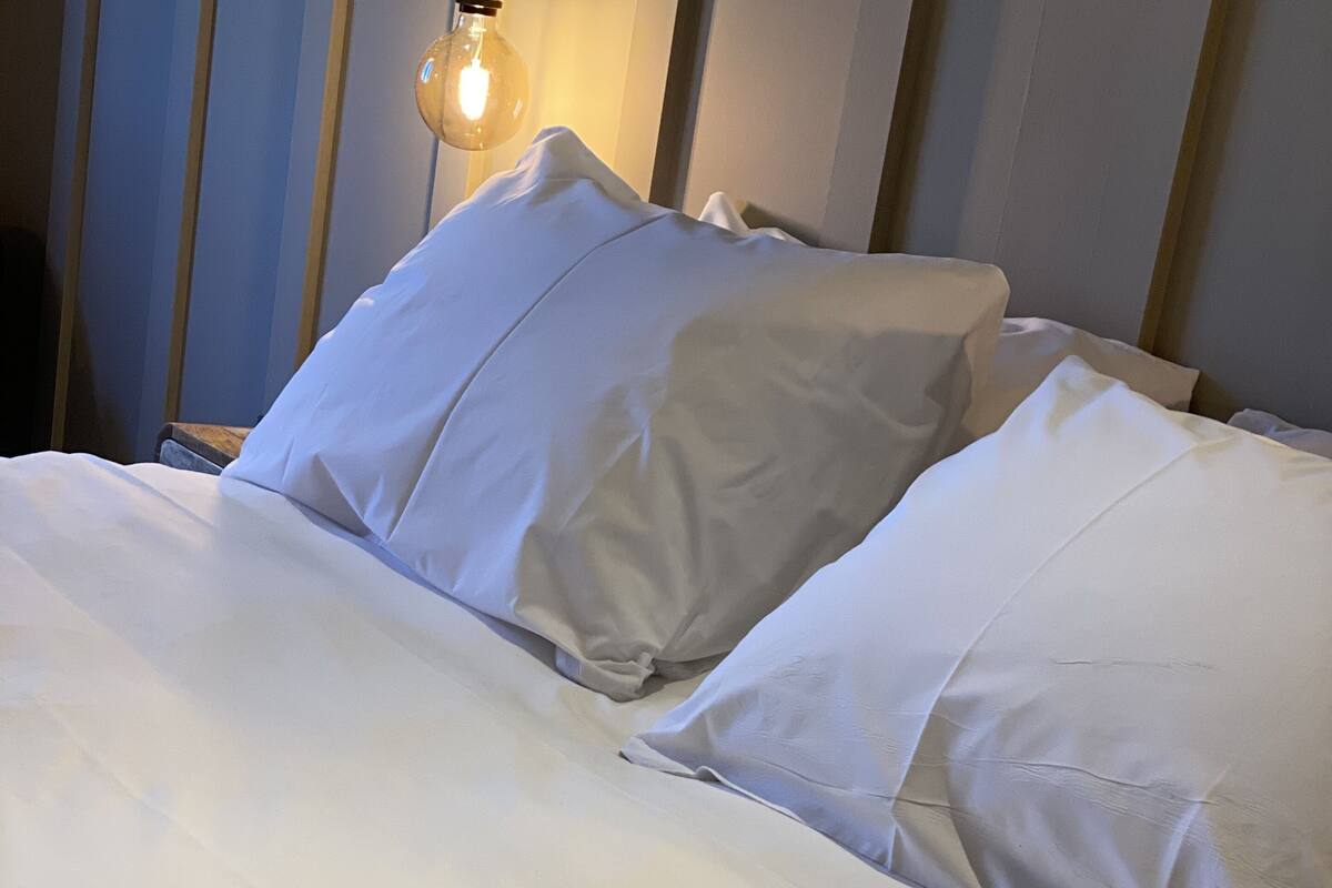 A neatly made bed with white linens and pillows, a bedside lamp, and a wooden headboard.