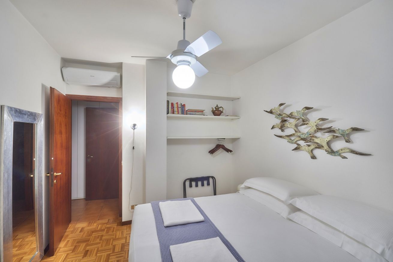 Ein Schlafzimmer mit Bett, Deckenventilator, einer Wandablage mit Büchern und einem dekorativen Wandbild.