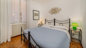 A bedroom with a bed, a window with curtains, a wall clock, and a framed picture.