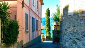 A narrow street with a pink building on the left and a stone wall on the right. - Casa Royal beautiful Garden (Varenna)