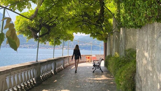 A paved walkway with a railing, a bench, and a person walking. - Casa Royal beautiful Garden (Varenna)