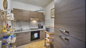 A compact kitchen with wooden cabinets, a gas stove, a microwave, and a refrigerator. - Casa Riva on the lakeshore (Varenna)