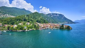 A coastal town with buildings along the waterfront, a small island with a church, and mountains in the background. - Casa Riva on the lakeshore (Varenna)
