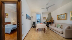 A well-lit living room with a sofa, a dining table, and a bed in the adjacent room. - Casa Riva on the lakeshore (Varenna)