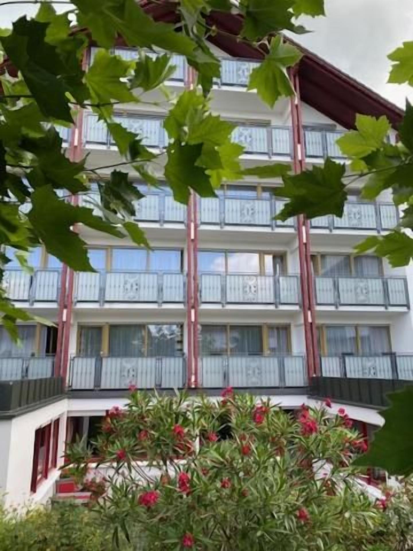 Un edificio de varios pisos con balcones y un jardín con flores rojas.