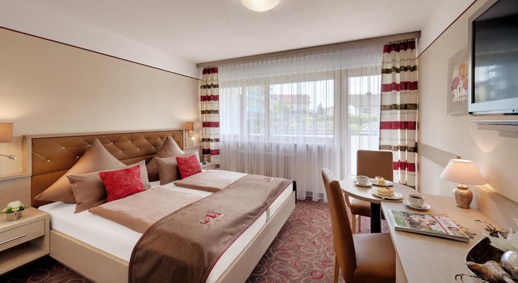 Ein Hotelzimmer mit einem großen Bett, einem Schreibtisch, einem Stuhl und einem Fernseher.