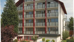 A multi-story hotel with balconies, a covered outdoor area, and a garden with seating. - Pension- Hotel Maximilian (Bad Fuessing)