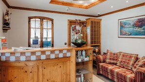 A reception area with a wooden counter, a glass display case, a couch, and a painting on the wall. - Pension- Hotel Maximilian (Bad Fuessing)
