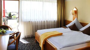 A hotel room with a bed, a desk with a chair, a lamp, and a view of the outside. - Pension- Hotel Maximilian (Bad Fuessing)