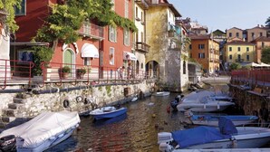 A narrow canal with boats docked on both sides, surrounded by colorful buildings with balconies and arches. - Wonderful Casa Veranda (Varenna)