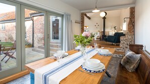 A dining area with a table set for four, a vase with flowers, and a view of the backyard through glass doors. - Spacious barn, seals, seaside walks and Broads National Park (Great Yarmouth)