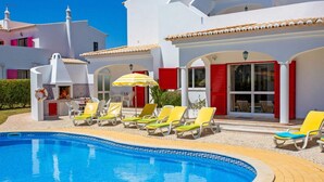 A swimming pool with sun loungers and umbrellas, surrounded by white buildings with red shutters. - Villa in Alporchinhos (Porches) within walking distance to the beach. (Porches)