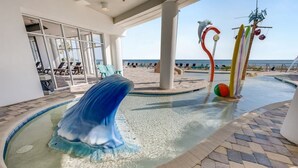 Un espace piscine agrémenté d’une sculpture de dauphin, de chaises longues et offrant une vue sur la plage.