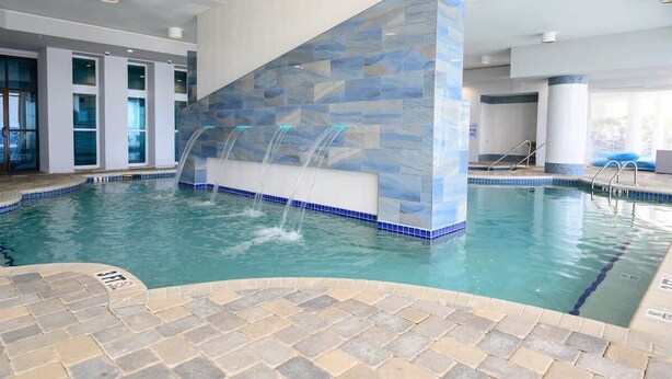 Une piscine intérieure dotée d’une cascade aux carreaux bleus et d’une eau d’un bleu limpide.