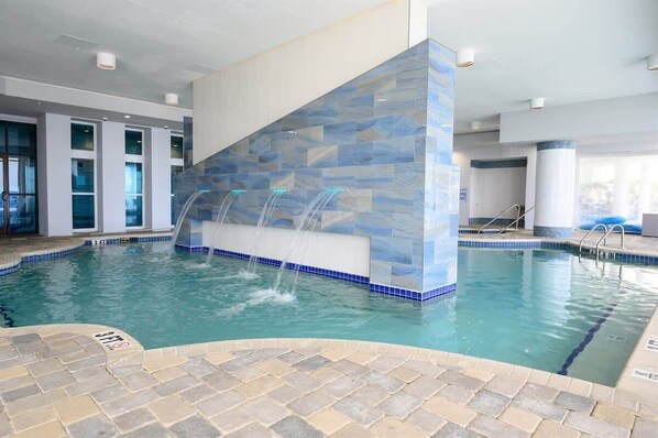An indoor swimming pool with a blue-tiled waterfall feature and a clear blue pool. - Direct Oceanfront Remodeled King 2BR,Amazing Views (Myrtle Beach)