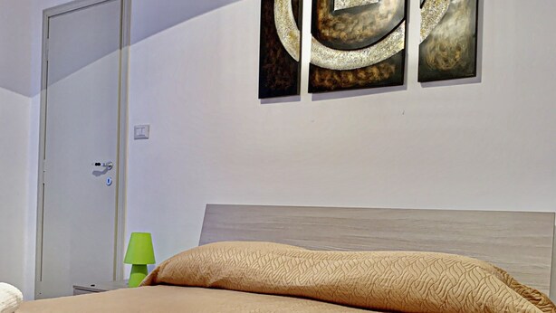 A hotel room with a bed, a door, and a wall with three artwork pieces. - Appartamenti Viale Italia (Sassari)