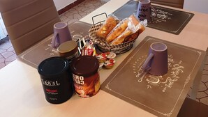 A dining table with a basket of bread, two cups, a jar of spread, and a container of yogurt. - Appartamenti Viale Italia (Sassari)