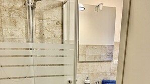 A modern bathroom with a glass-enclosed shower, a white sink, and a marble-tiled wall. - Appartamenti Viale Italia (Sassari)