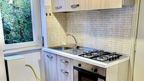 A compact kitchen with a gas stove, oven, and a window with a view of greenery. - Appartamenti Viale Italia (Sassari)