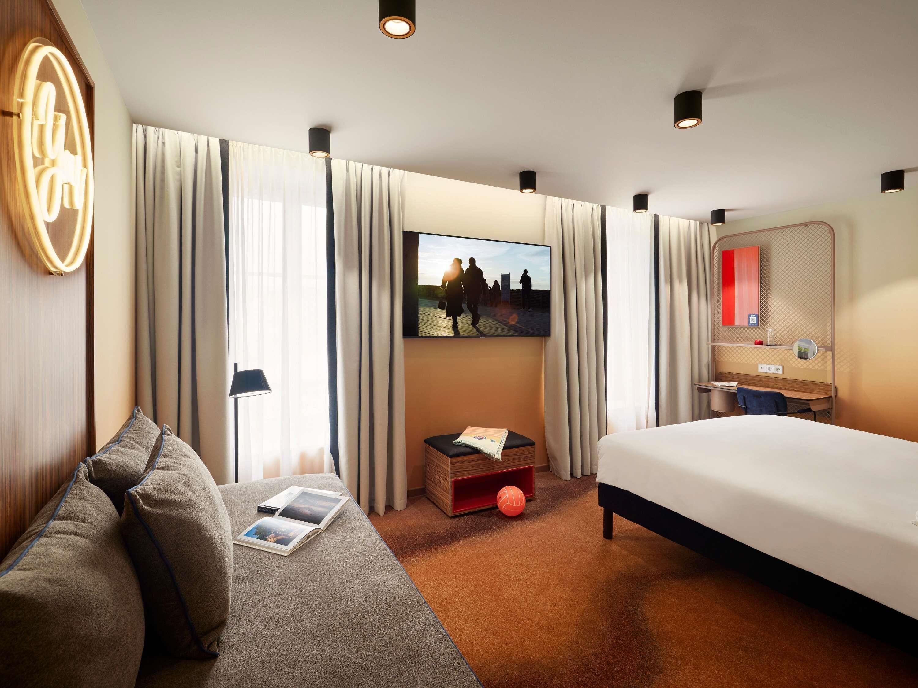 Habitación de hotel con cama, sofá, televisor, escritorio y espejo.