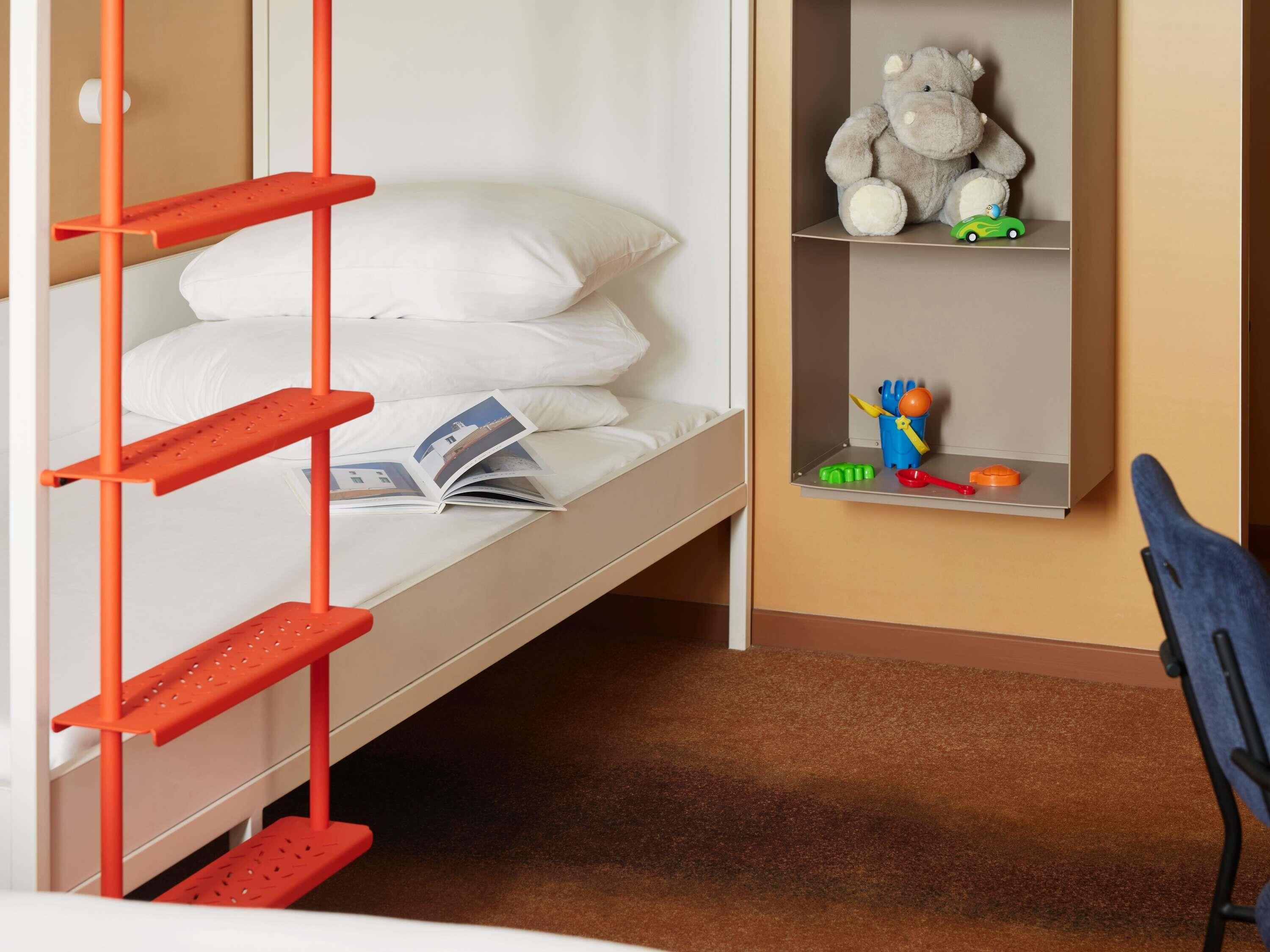 A bunk bed with a red ladder, a shelf with toys, and a chair.
