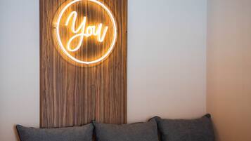 A modern room with a wooden accent wall, a neon sign reading "You", and a grey sofa with two cushions.