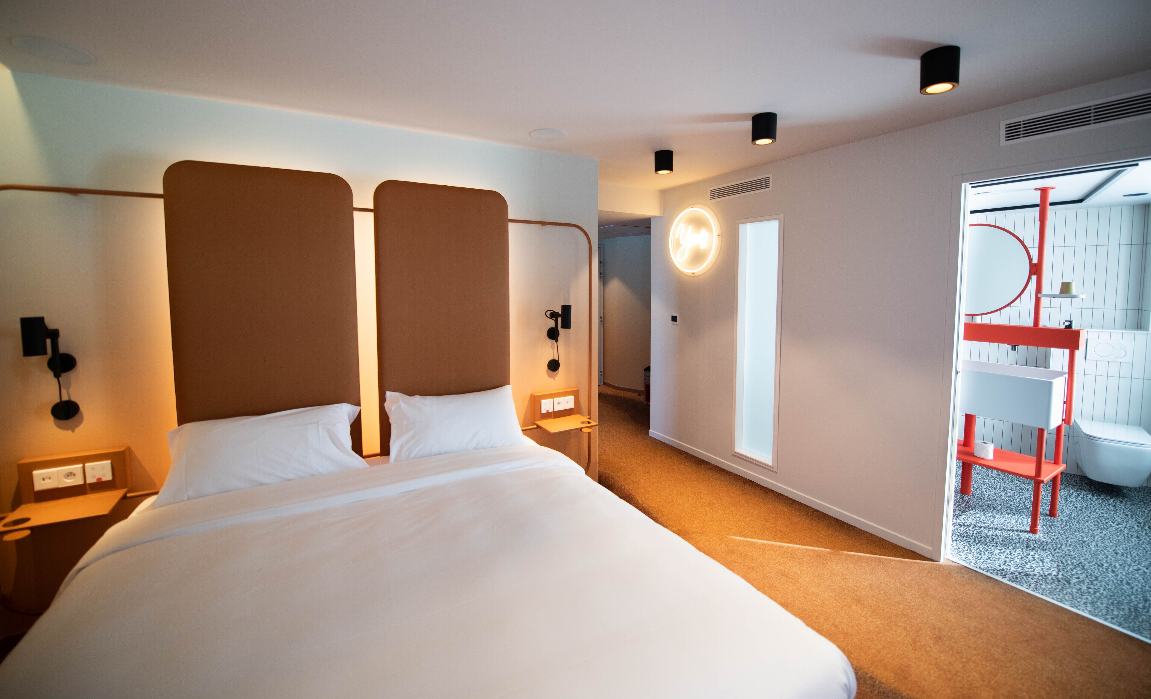 Una habitación de hotel moderna con una cama grande, mesitas de noche, un teléfono en la pared y un baño visible a través de una puerta abierta.