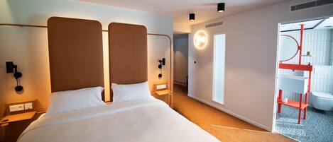 Una habitación de hotel moderna con una cama grande, mesitas de noche, un teléfono en la pared y un baño visible a través de una puerta abierta.