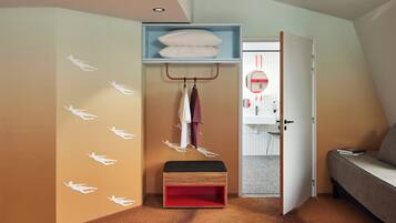 A bedroom with a bed, a bench, a shelf with pillows, and a door leading to a bathroom.