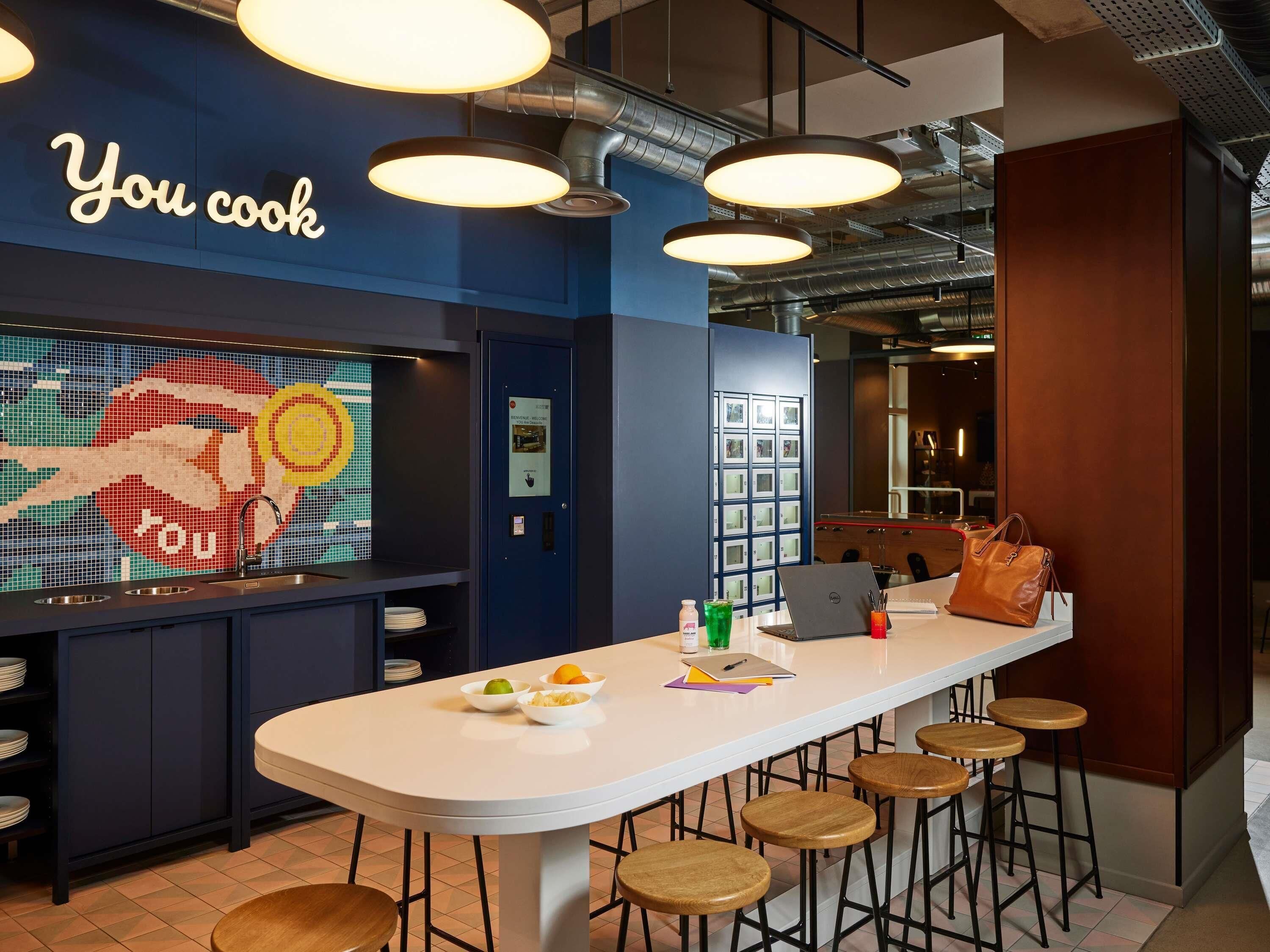 A modern kitchen area with a bar counter, stools, and a wall with a 'You cook' sign.