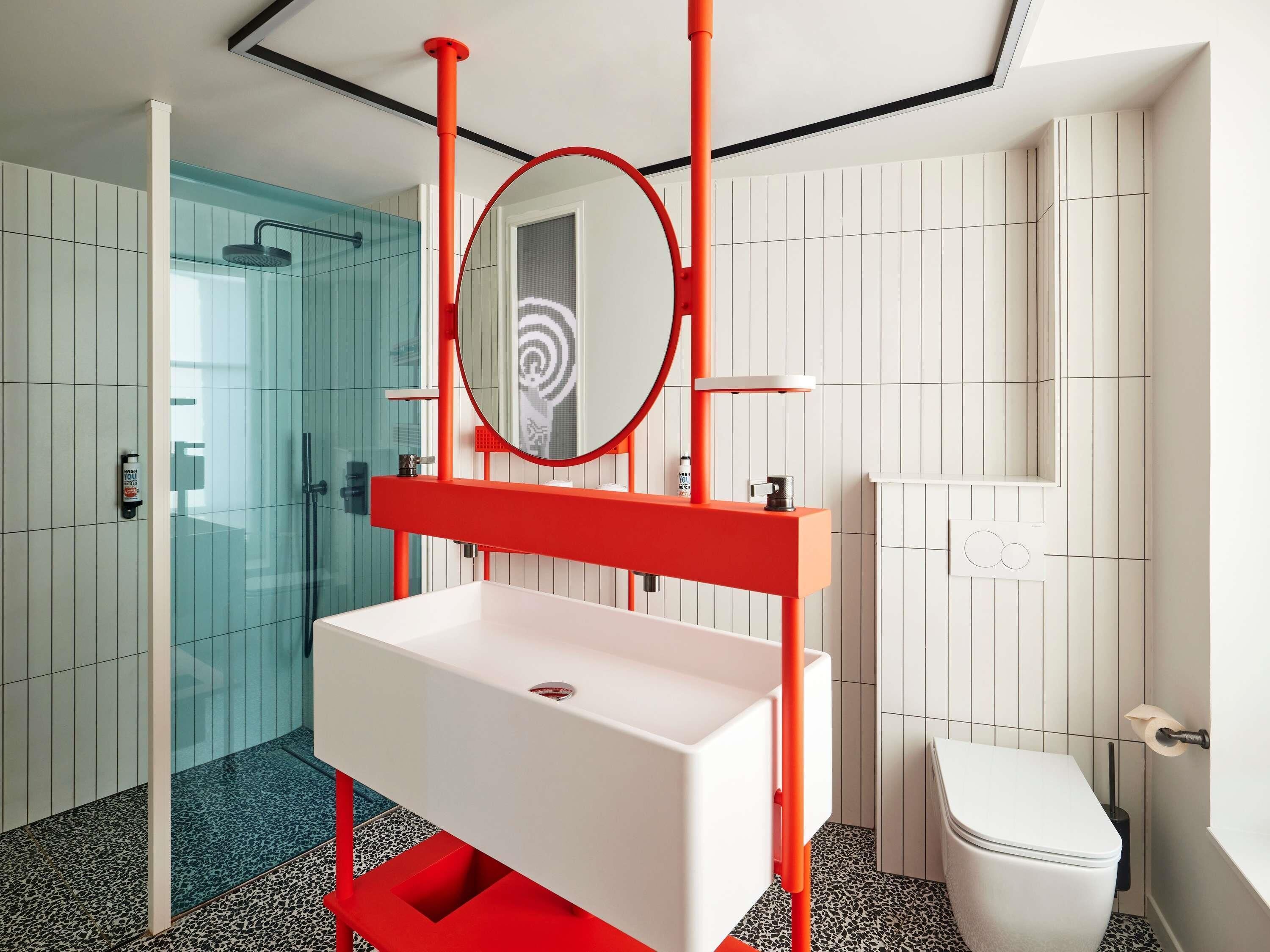 A modern bathroom with a white sink, red accents, a glass shower enclosure, and a white toilet.