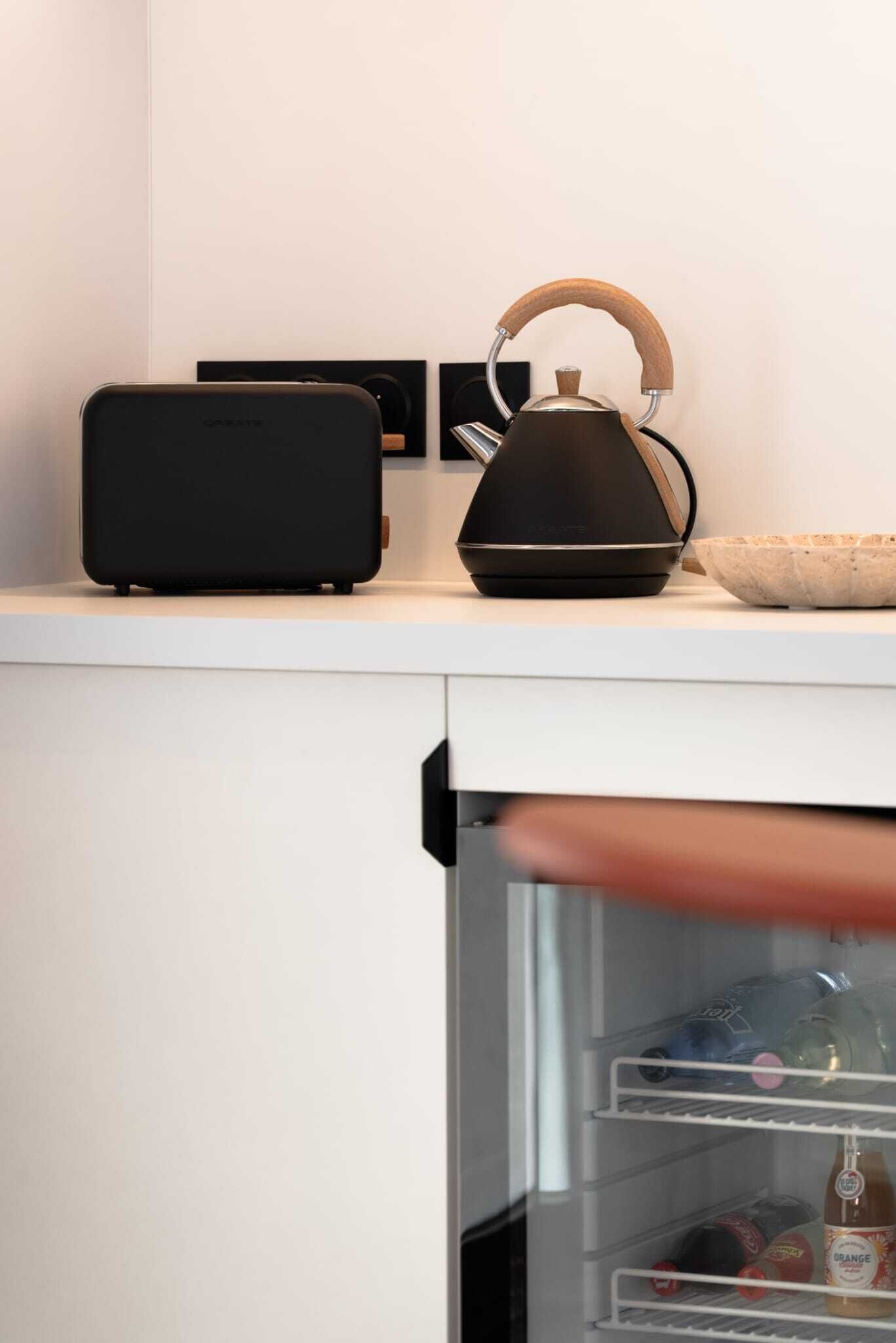 Een keukenhoek met een waterkoker, een zwarte speaker en een kom op het aanrecht.