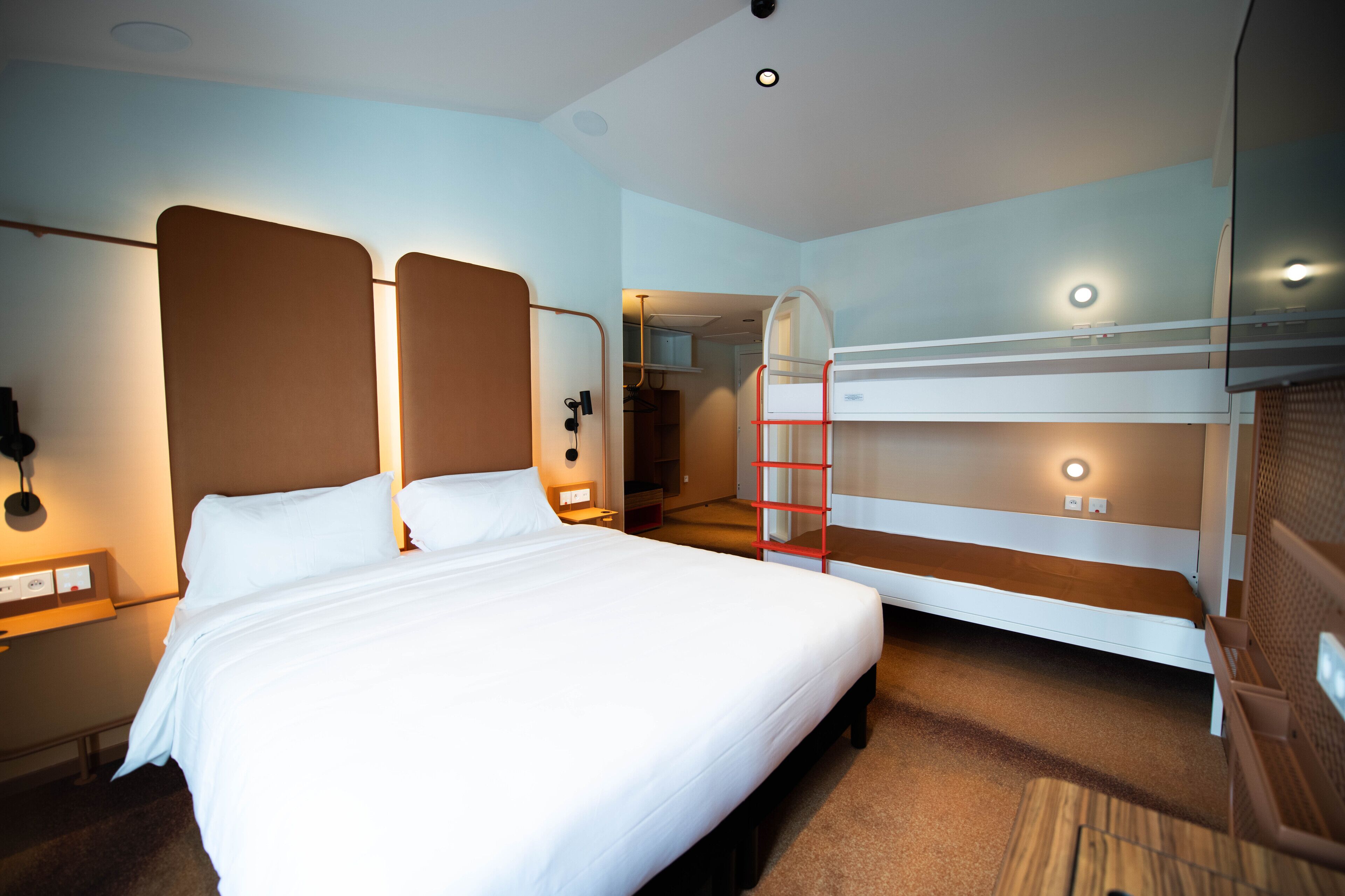 A hotel room with a large bed, a bunk bed, a desk, and a nightstand.