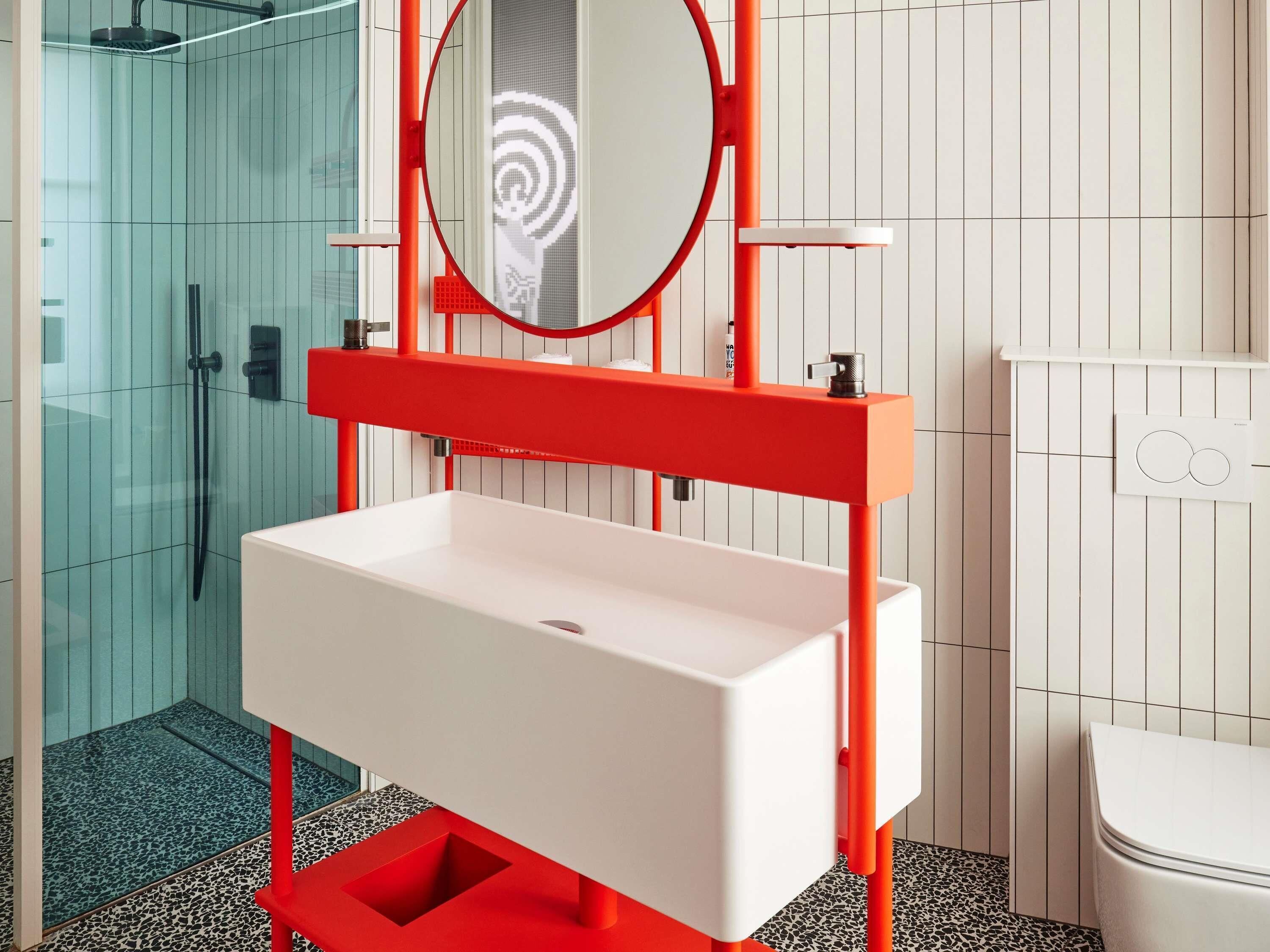 A bathroom with a white sink, red accents, a glass shower enclosure, and a white toilet.