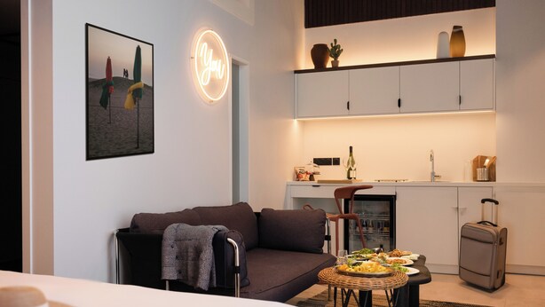 Una sala de estar moderna con un sofá, una mesa de comedor con comida, una zona de cocina y una maleta.