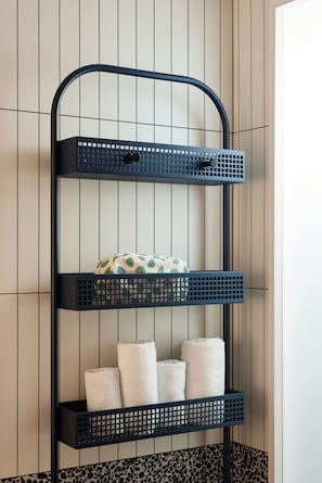 Une étagère en métal noir à trois niveaux, chaque niveau étant utilisé pour ranger des serviettes et un coussin à pois.