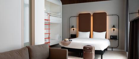 A modern hotel room with a bed, a sofa, a small table with a cup, and a suitcase.