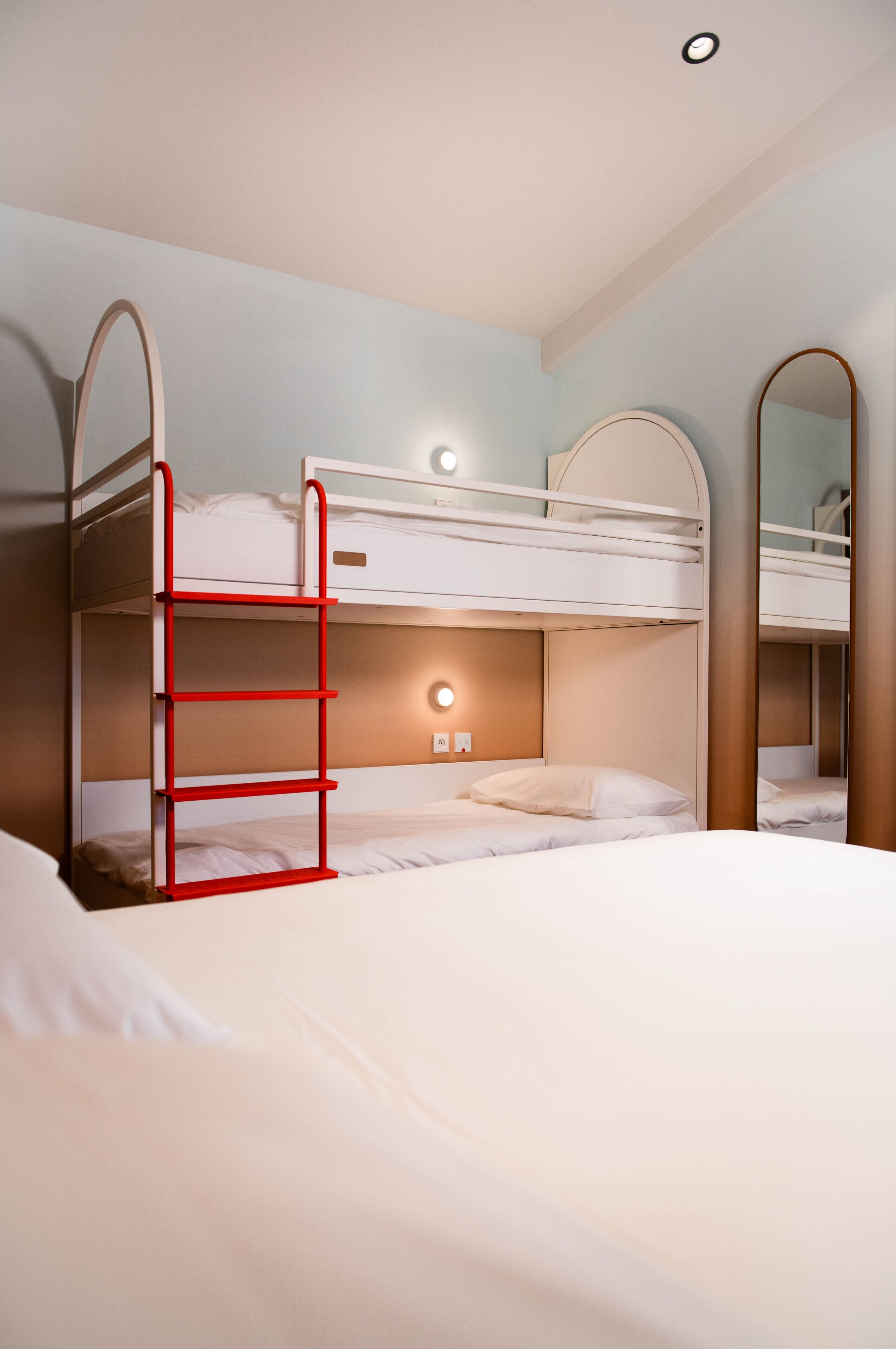 A bunk bed room with a red ladder, a bedside table, and a mirror.