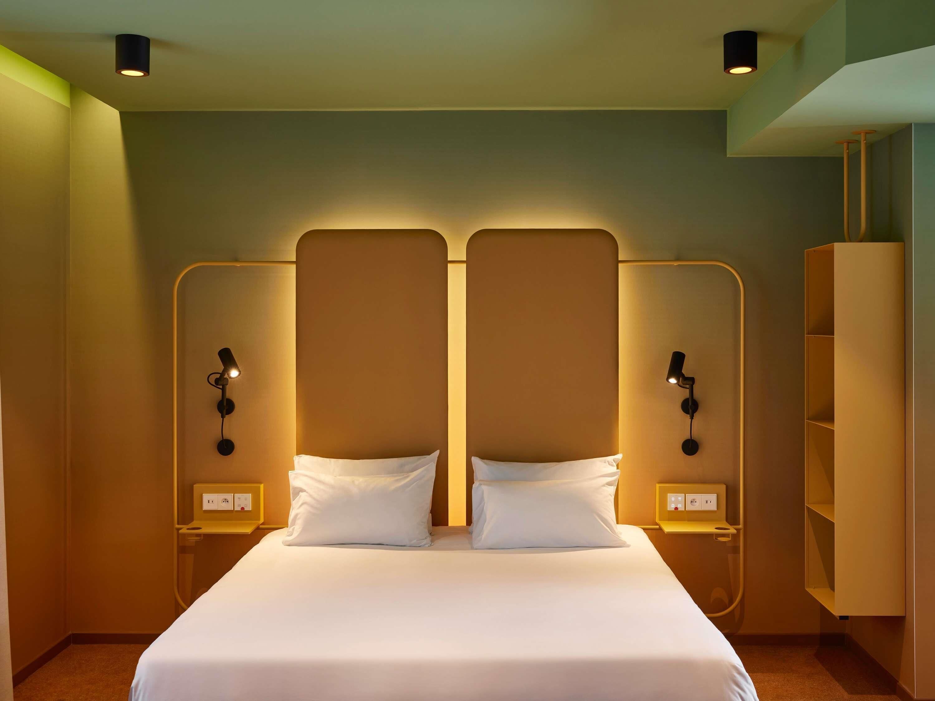 A hotel room with a large bed, two bedside tables, and a wardrobe.