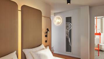 Une chambre d’hôtel moderne équipée d’un lit, d’un téléphone fixé au mur, d’un néon et d’une fenêtre donnant sur l’intérieur de l’hôtel.